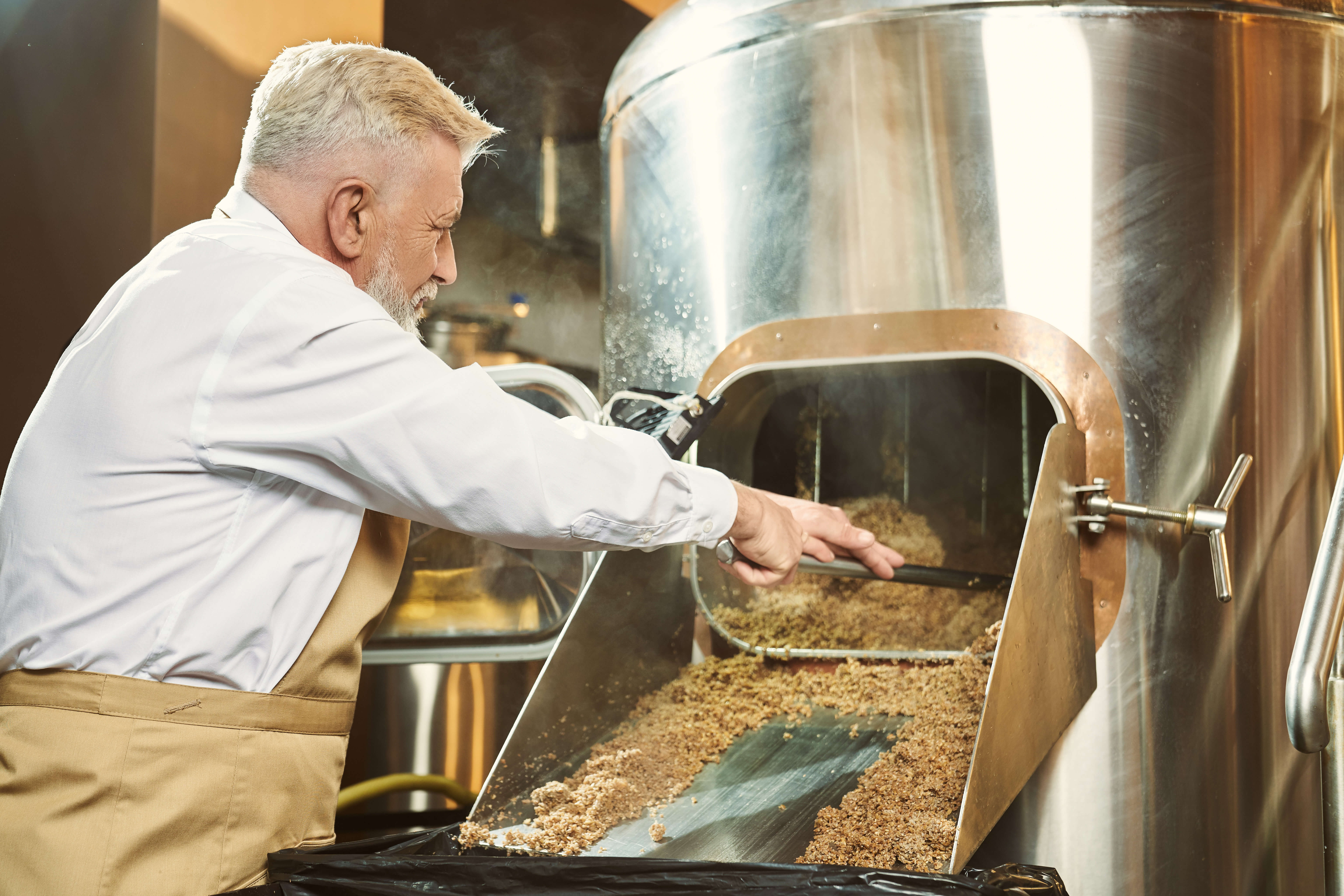 Brewery worker getting spent grain with shovel