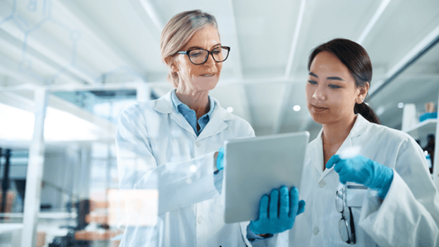 Two female scientists in lab coats reviewing data on a tablet in a modern laboratory.