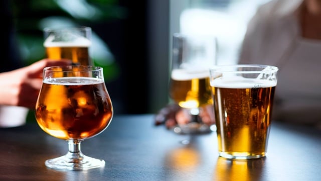 Four glasses of beer on a dark table, showing different beer styles with golden and amber colors in a casual indoor setting.