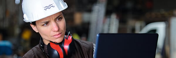 Female engineer wearing hard hat and hearing protection looking at laptop